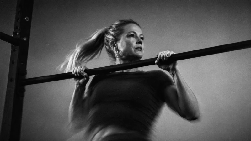 Een vrouw doet een pull-up aan een stang in een sportschool, gefotografeerd in zwart-wit.