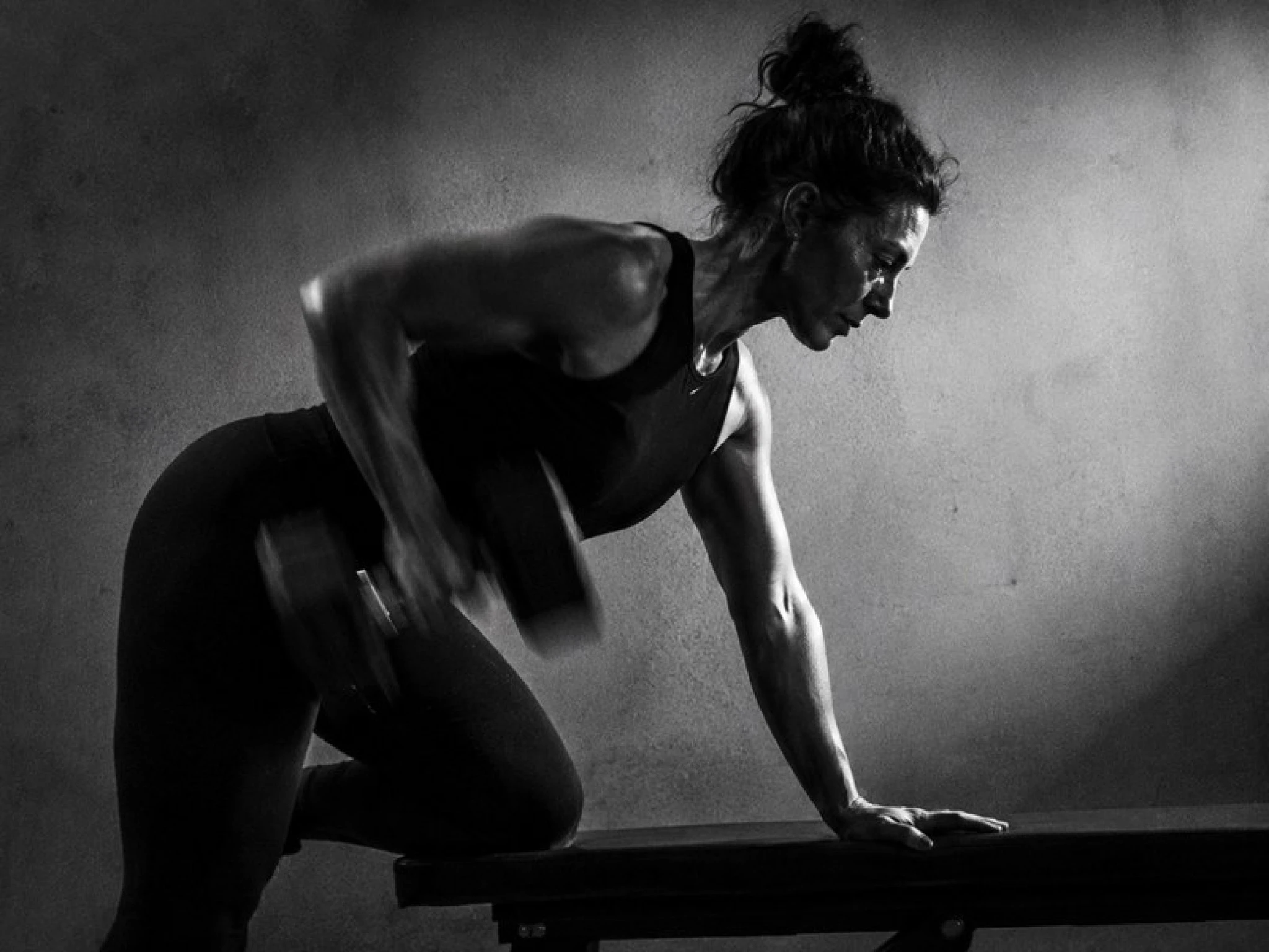 Vrouw midden in een herhaling met een dumbbell, arm onscherp door de beweging.