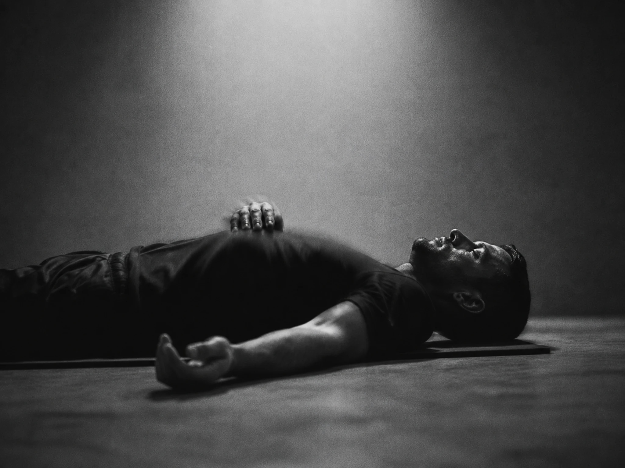 Man ligt op zijn rug op een mat in een donkere studio, ogen dicht, herstellend na de training.