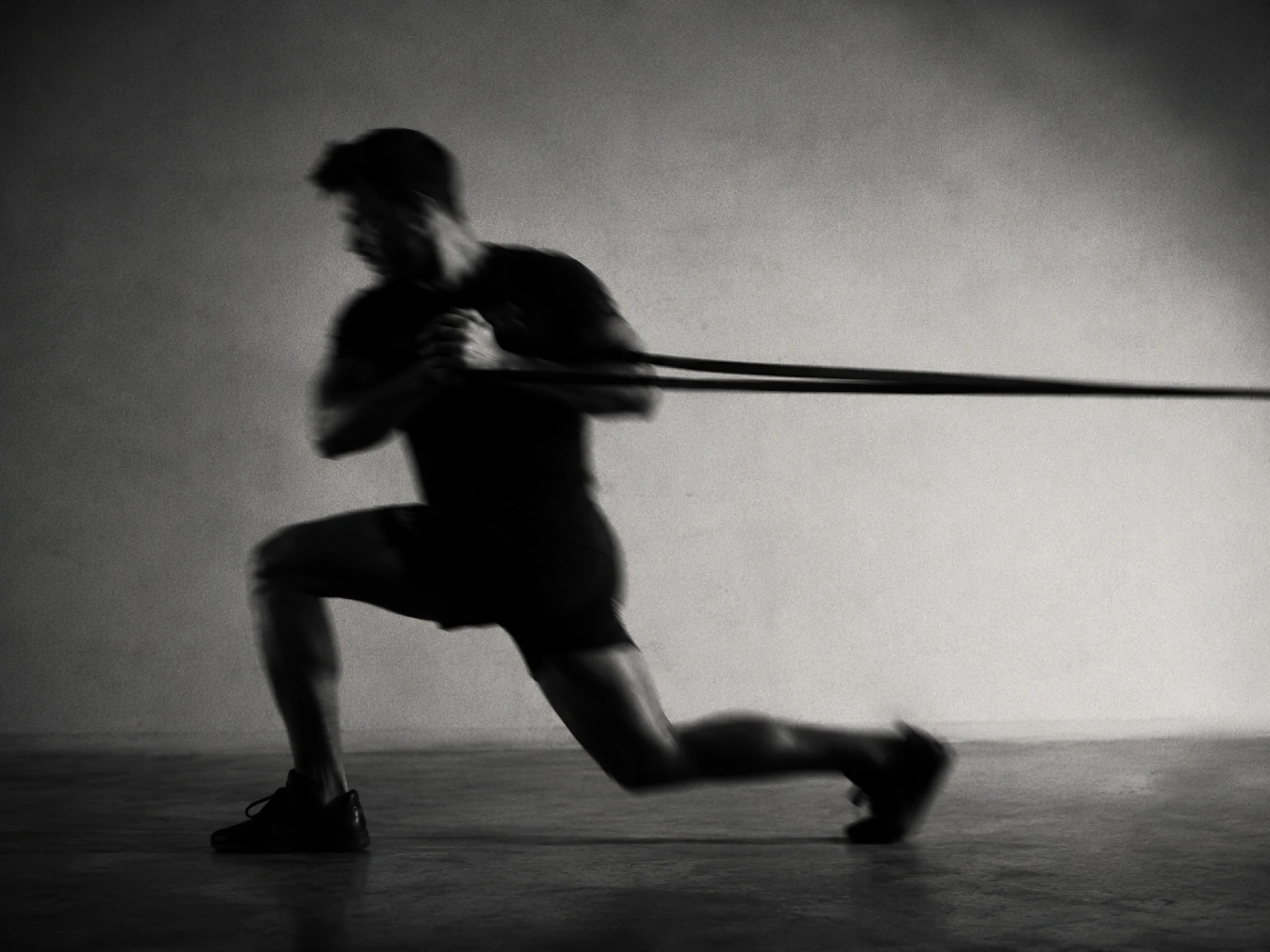 Athlete in a split squat holding off the lateral pull of a resistance band, black and white.