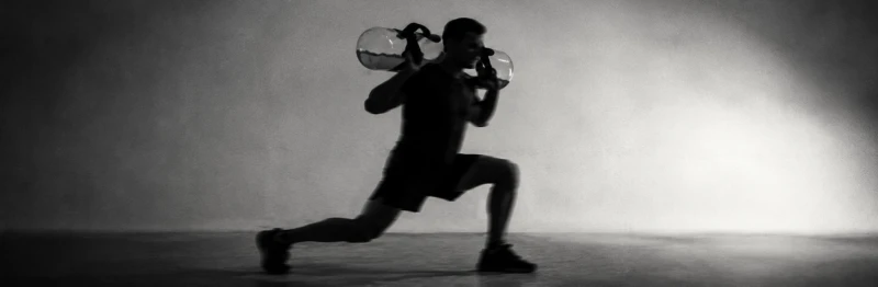 Athlete in a lunge with an aquabag across the shoulders, black and white with motion blur.