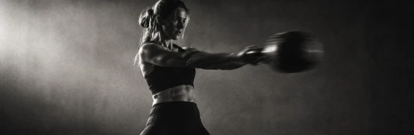 Woman performing a heavy kettlebell swing in a dark studio