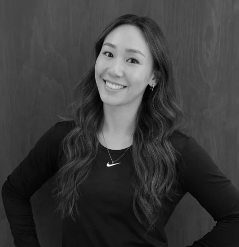 Ani McNally - een vrouw met lang haar glimlacht, draagt een zwart shirt met een Nike-logo en staat voor een effen achtergrond.