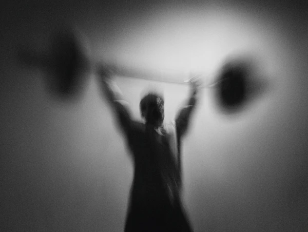 Foto met bewegingsonscherpte. Je ziet een man die een stang met twee gewichten omhoog tilt