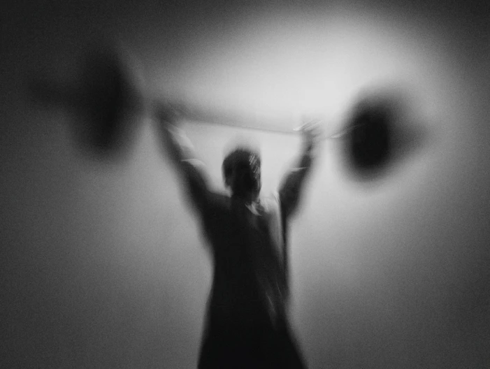 Foto met bewegingsonscherpte. Je ziet een man die een stang met twee gewichten omhoog tilt