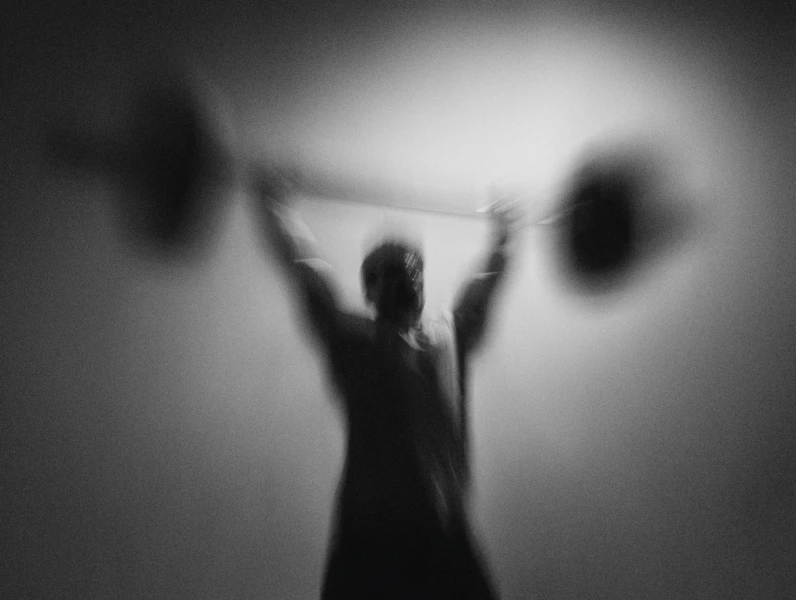 Foto met bewegingsonscherpte. Je ziet een man die een stang met twee gewichten omhoog tilt